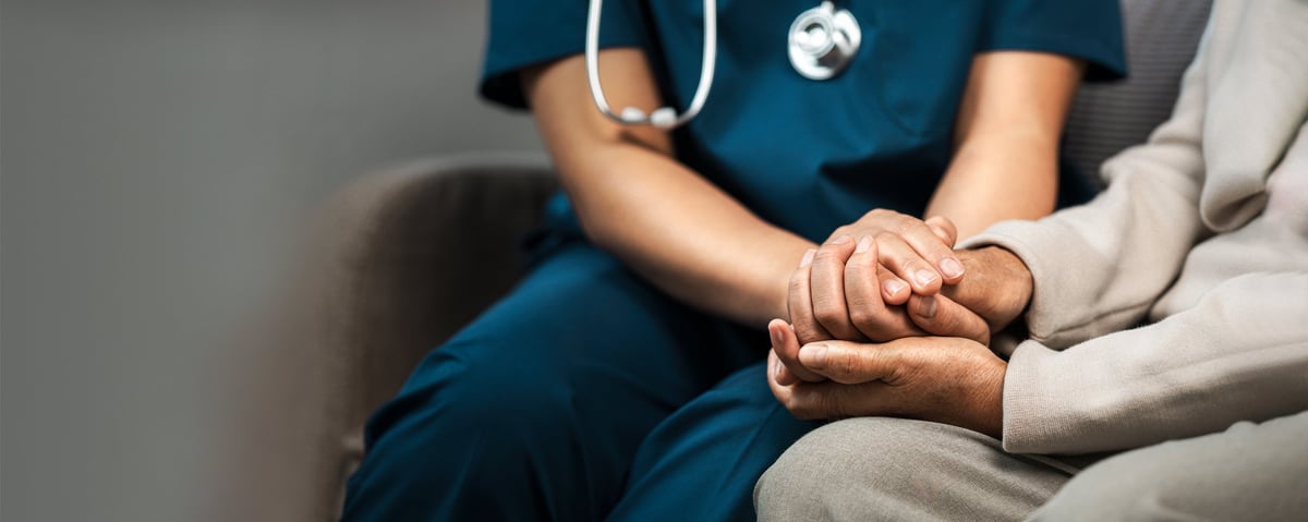 A caregiver holds hands with an elderly woman to offer comfort