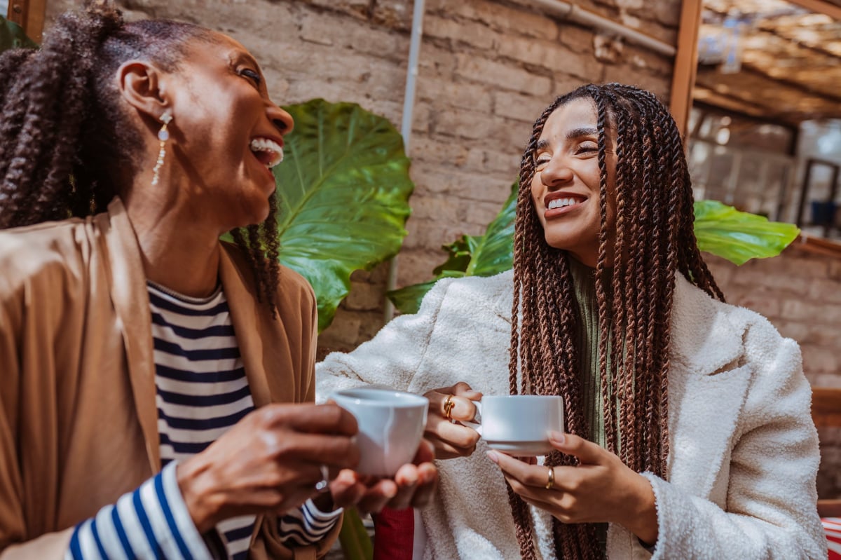 Two Black women friends share a laugh together over coffee
