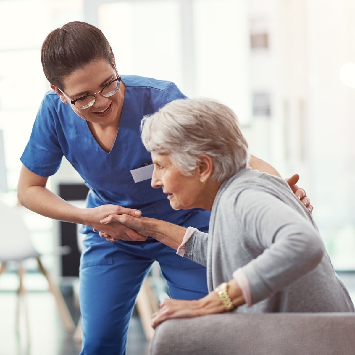 A caregiver gently helps a senior patient up from a chair